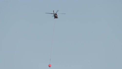Helicopter Carrying Water Bucket in Clear Blue Sky