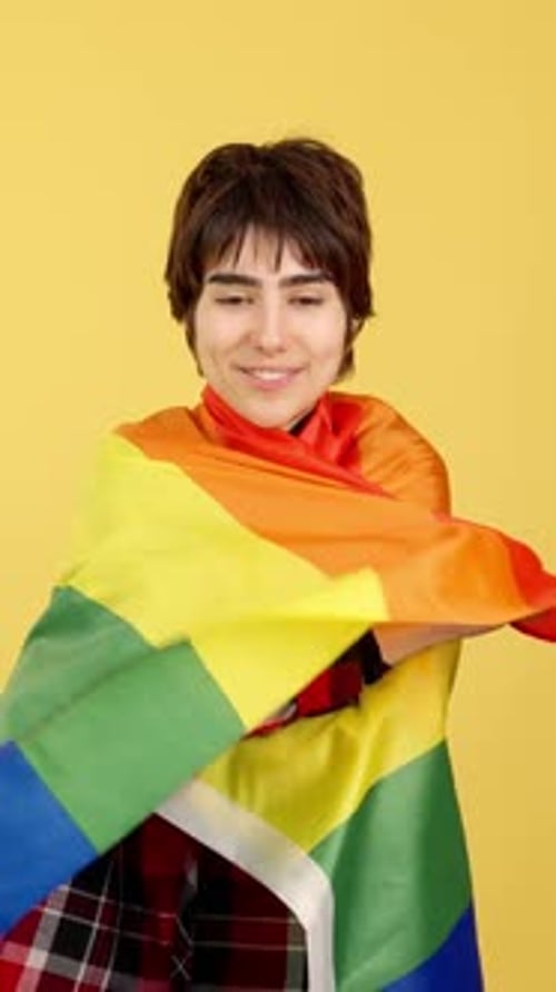 Young adult smiles wrapped in pride flag