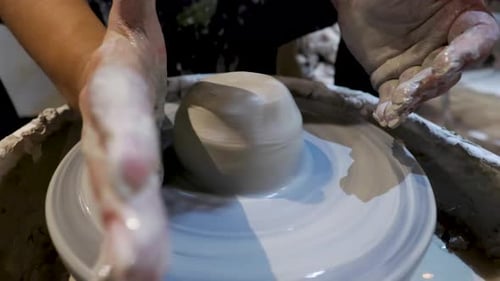 side view of an African American hands spinning clay very sporadically while the wet molded clay mo