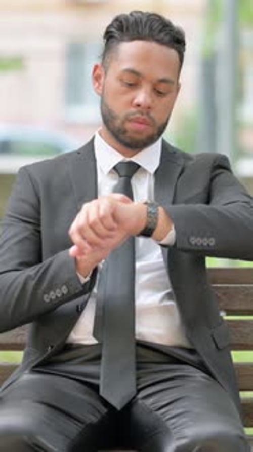 Well-dressed Man Checks Watch While Sitting on Bench