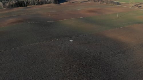 White radio control plane flying over brown fields. Drone shot in UHD.