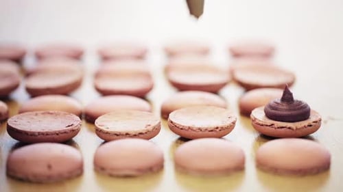 Female chef squeezing cream filling into macarons at a french pastry shop