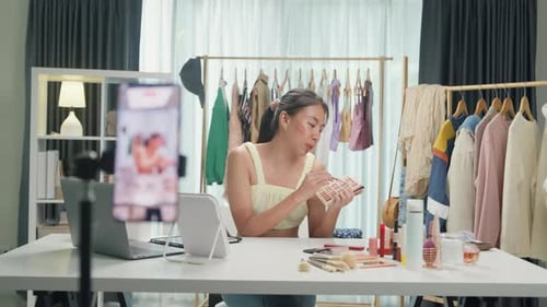 Asia lady blogger look phone camera recording swatch apply eye shadow palette on skin show review.