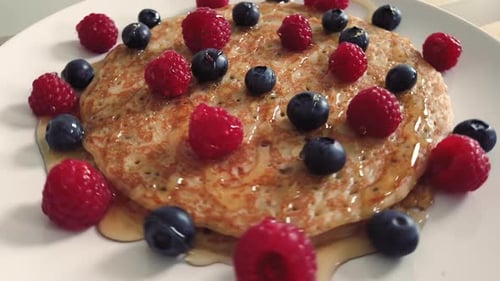 Spinning stack of pancakes with raspberries, blueberries and honey