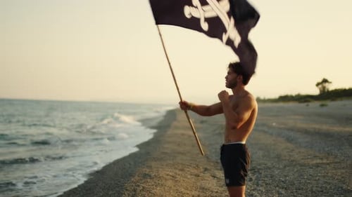 Shirtless Man Waving Pirate Flag on Beach