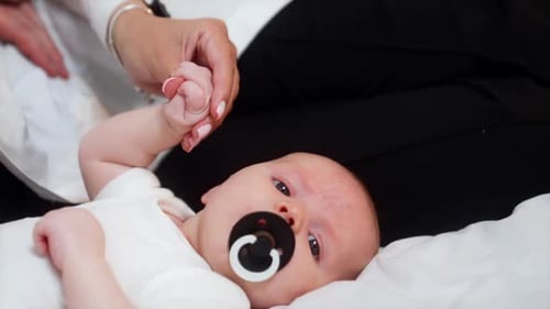 Lovely newborn with a pacifier in mouth. Mom holds a tiny baby hand. Close up.