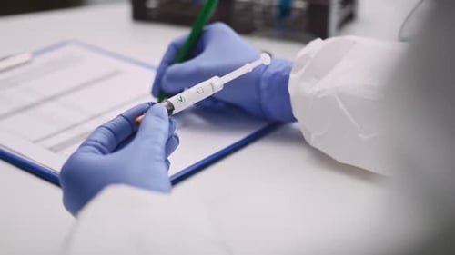 Gloved Hand Marks COVID-19 Vaccine Vial in Lab