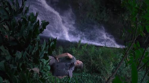 Rear view of male traveler standing in front of waterfall.
