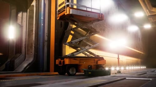 Orange Scissor Lift Positioned Indoors in Industrial Space with Bright Lights