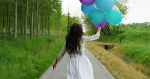 Girl Runs Down Path Holding Pastel Balloons