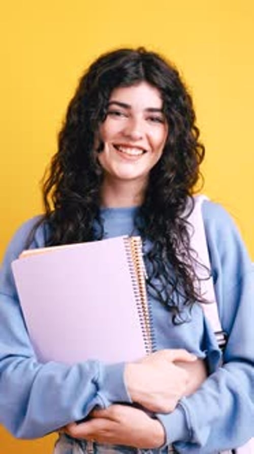 Smiling Young Woman Holding Notebooks on Yellow Background