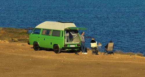 Group of People Relaxing in Nature with a Motorhome Standing on a Cliff Above the Sea Holiday in a