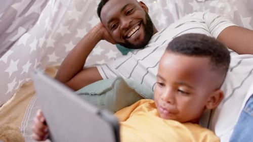 Happy african american father and son using tablet and smiling at home, slow motion