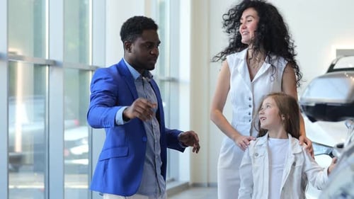 African American Dealer Shows Car to Customer with Daughter