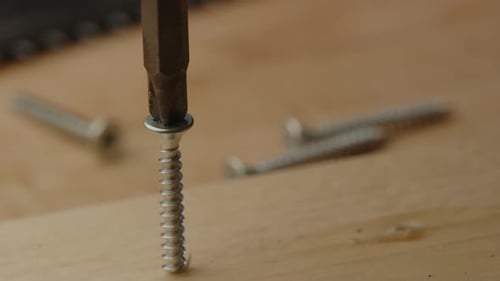 view of electric screwdriver drilling screw in wooden board on a construction site in slow motion