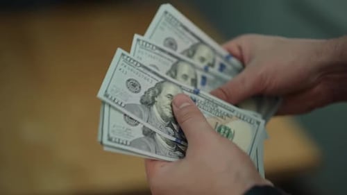 Vista aproximada de mãos segurando e contando notas de $100.