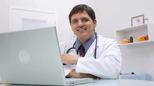 Smiling Male Doctor at Desk with Laptop