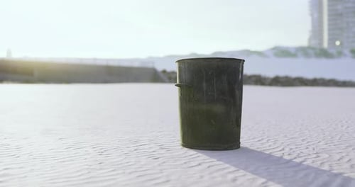 A Solitary Trash Bin Stands on a Sunlit Sandy Beach During Early Morning Hours