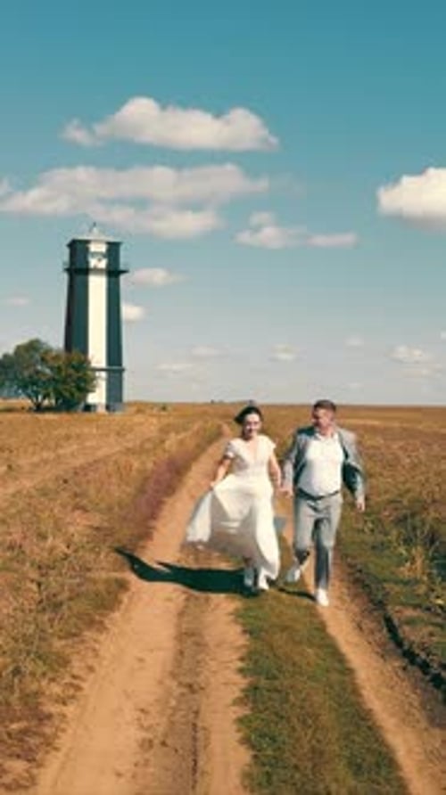 Two Happy Young People Running Together Holding Hands in a Field Lighthouse in the Field