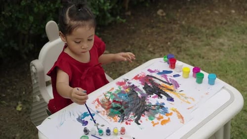 happy toddler girl painting watercolor in a paper at backyard