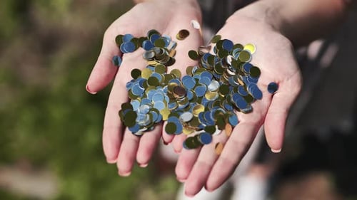 Hands Holding Gold and Blue Confetti Outside