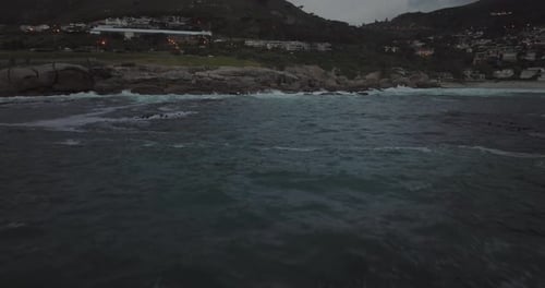 Drone flying over the sea at Camps Bay beach in Cape Town South Africa - It's cloudy and the waves a