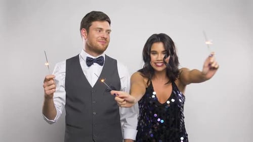 Happy young couple celebrates with sparklers in studio