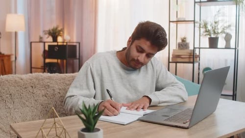 Young Adult Working from Home Writing in Notebook