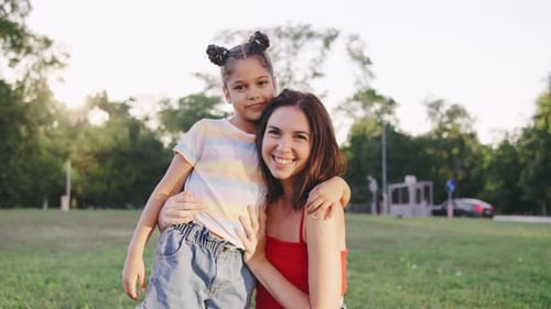 Smiling Woman and Her Daughter Enjoying a Sunny Day in a Park Surrounded By Greenery and Softly Lit