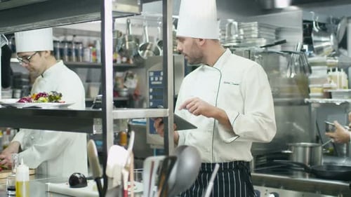 Professional chef in a commercial kitchen in a restaurant or hotel is using a tablet computer.