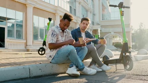 Two Friends Having Fun Drinking Coffee with Shared Electric Push Scooters in the City