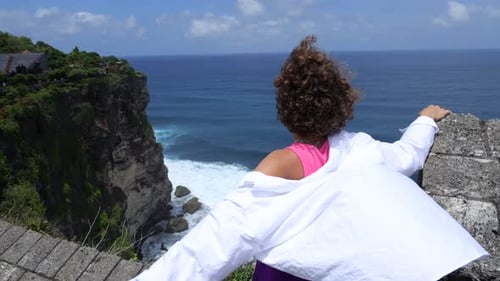 Vista trasera de una mujer en un mirador elevado Una joven caucásica de pelo rizado mira las olas del mar desde