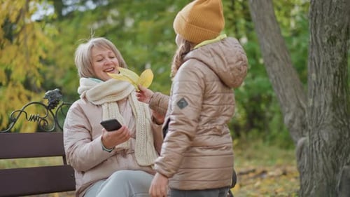 Woman Gathering Leaf Hugging Daughter on Autumn Park Bench