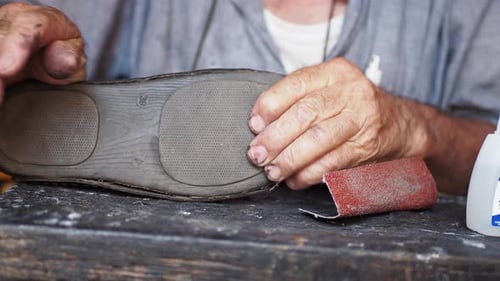 Un cordonnier qui répare des chaussures à l'aide d'une aiguille