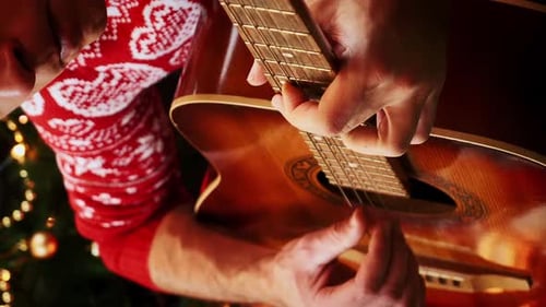 Man Plays Guitar by Christmas Tree at Night