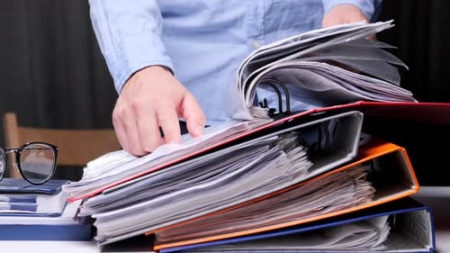Office Worker Studies a Contract Document in the Archive Stack of Binders
