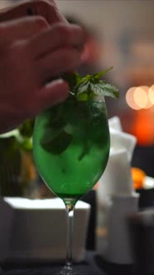 Bartender is making green summer cocktails with fresh mint leaves and lime