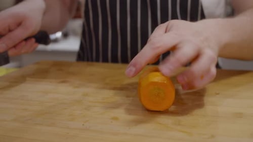 Chef cuts carrot into pieces on wooden cut board. Close up on hands. Slow motion.