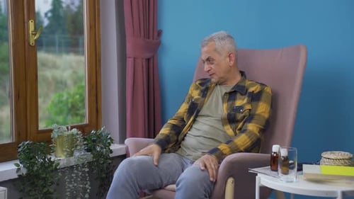 Man Rubs Sore Shoulder Inside Home by Window