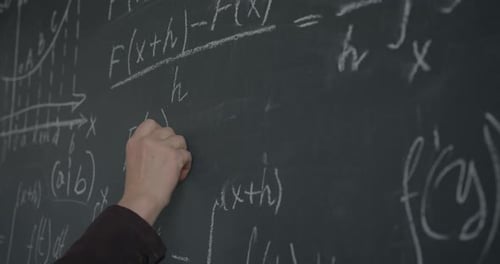 Closeup of Male Hand Writing Mathematics Formula on Chalkboard While Professor Working at Theory in