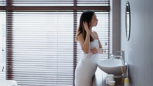 Woman in Towel Touches Hair in Bathroom