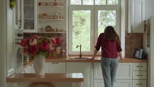Woman Standing in Bright Kitchen Looking out Window