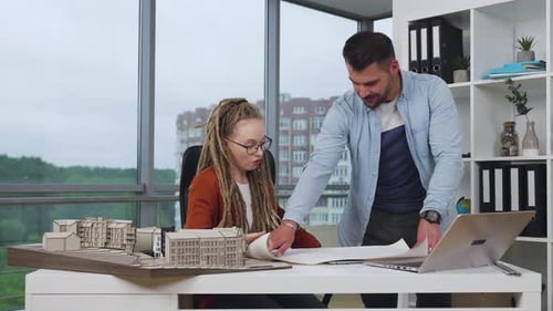 Woman and man architects go over blueprint of future buildings in modern design office