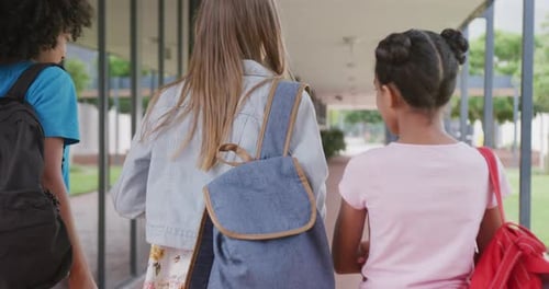 Video of rear view of three diverse schoolgirls walking in school corridor talking, copy space
