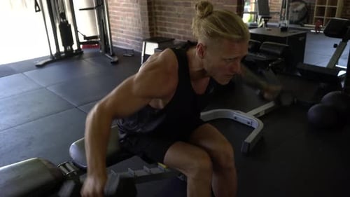 Tattoo man muscles in home gym doing seated dumbbell shoulder lateral raise