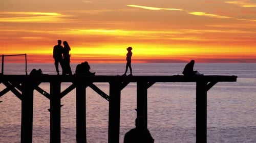 Silhouettes of Young People on the Sea Pier at Sunset