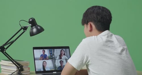 Young Asian Male Waving Hand For Greeting And Speaking While Studying By A Laptop On Green Screen