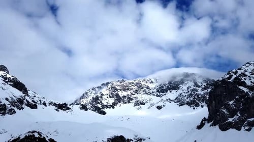 Timelapse camera with static camera of snowy mountains with blue sky and moving clouds rolling over
