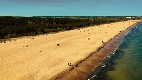 Sandy Beach with Gentle Waves and People Relaxing Green Forest Separating Coastline From City