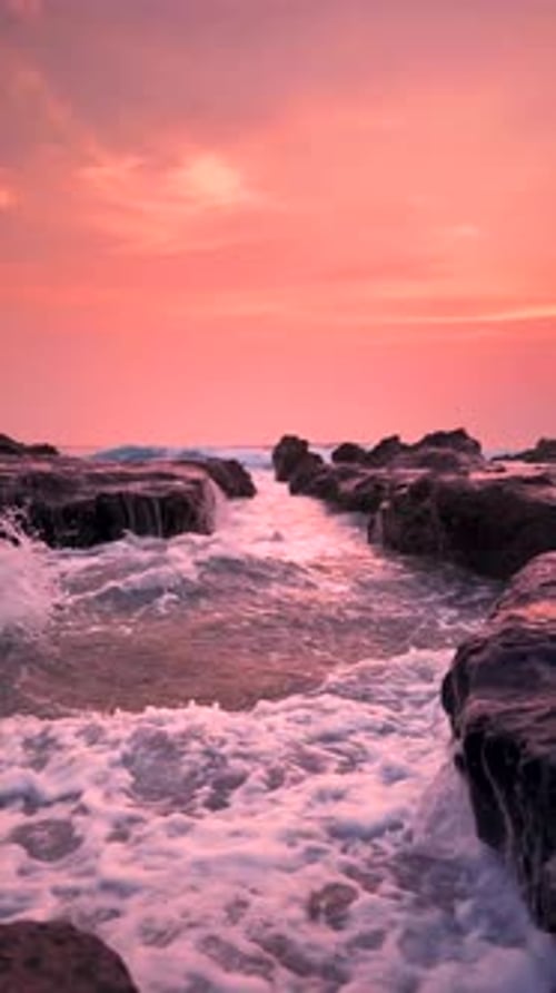 Kleine Wellen des Meeres, die die felsige Küste erreichen, und im Hintergrund der helle Sonnenuntergang